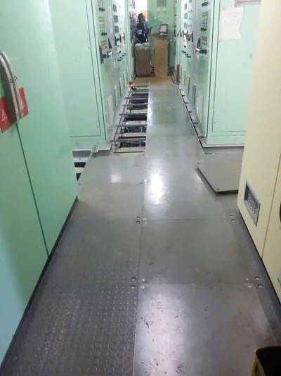 Passagem em sala técnica com piso elevado e quadros elétricos